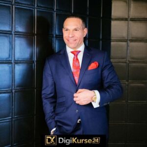 Marc Galal in schickem Anzug mit roter Krawatte und rotem Tuch in der Sakotasche vor einer schwarz gekachelten Wand.